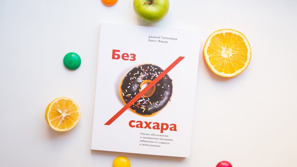 Top view of various fresh fruits and colorful magnet arranged on white background with book about proper nutrition